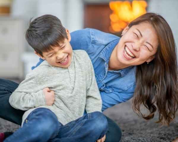 Mother sitting happily with her toddler, holding him from behind — a warm moment in their parenting journey.