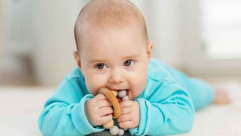 Adorable baby enjoying tummy time, grasping a colorful toy and putting it in mouth, exploring and learning.