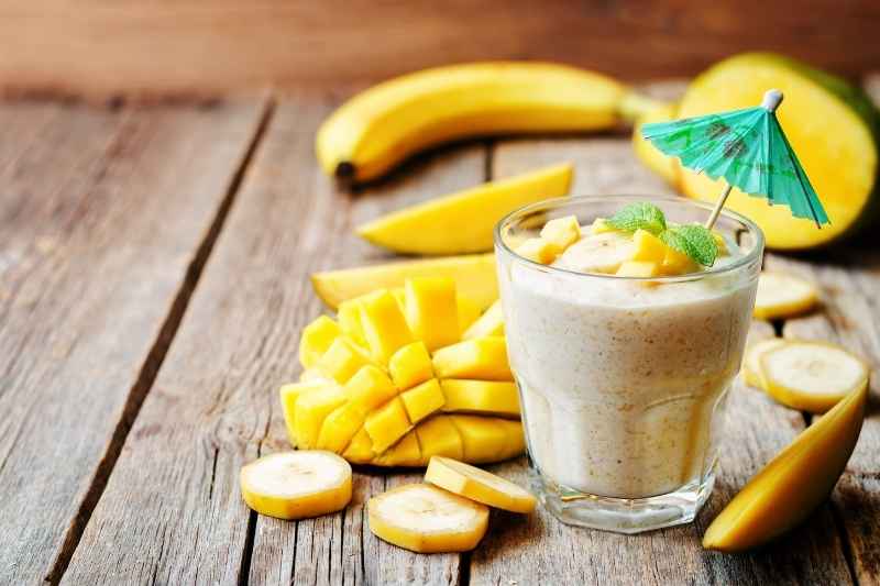 A bright color tropical mango and banana smoothie in a glass jar, ready for toddlers to enjoy.