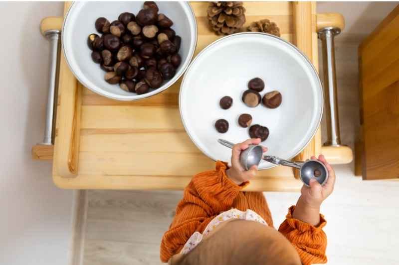 A little baby girl playing with a sensory bin bowl during a Montessori activity, exploring textures and objects. 