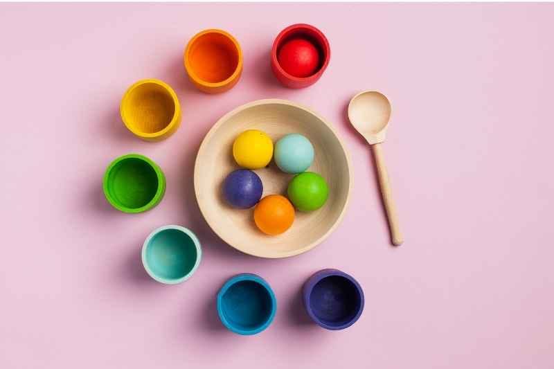 Montessori games for color sorting game with balls, cups, spoon, and a bowl to develop motor and cognitive skills. 