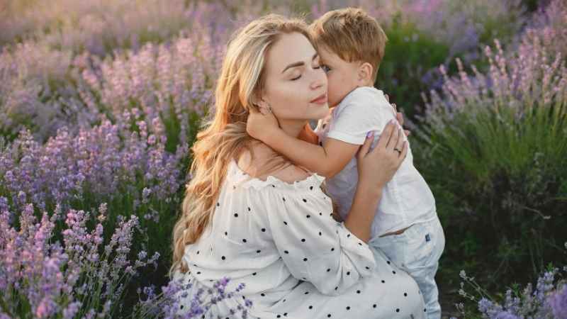 Mom and her young son in a flower garden at sunset, the little boy whispering 'Mommy' to his mother — a magical moment marking the baby’s first word.