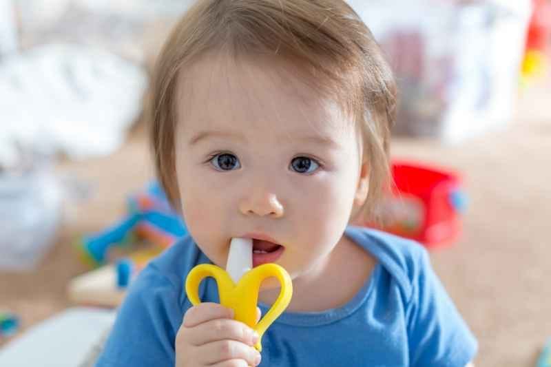 Baby holding banana-shaped Silicone Teether by Itzy Ritzy with easy-grip handles for soothing sore gums.