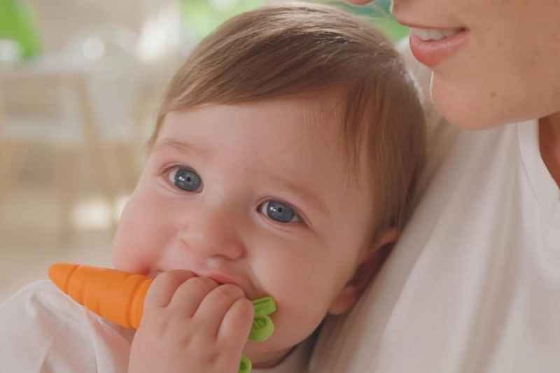 Baby playing with carrot-shaped Silicone Teether by Nuby, designed to soothe sore gums safely and comfortably.