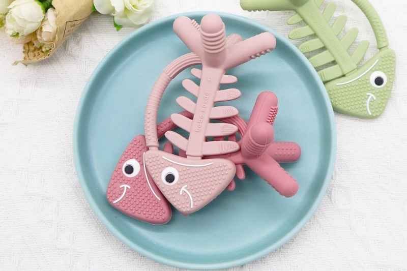 Two fish-shaped Silicone Teething Toys placed on a silicone baby food plate, designed to soothe and entertain teething babies.
