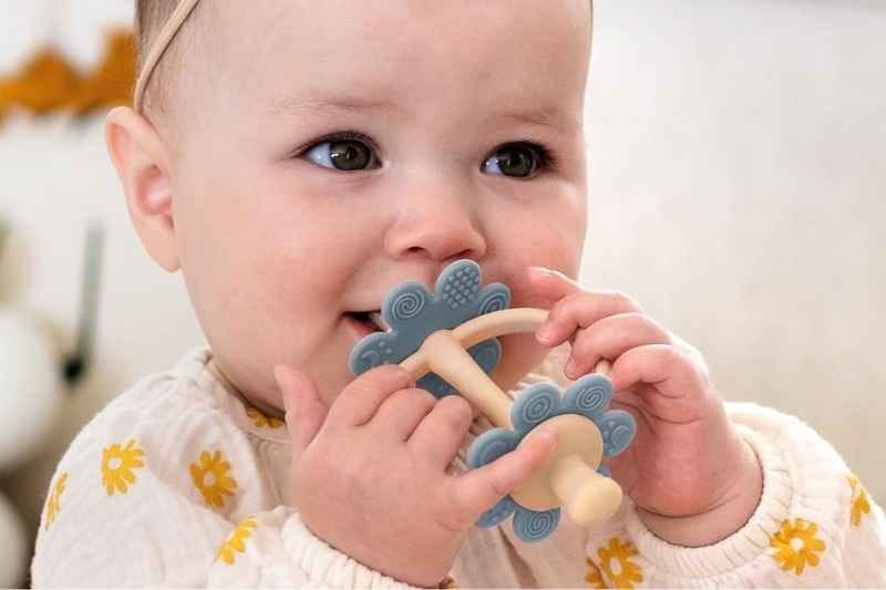 Baby girl holding a toothbrush-style Silicone Teething Toys by haakaa with a 360° baby toothbrush head in sky blue, soothing gums safely.
