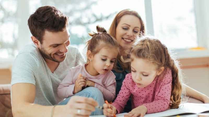 Happy family spending quality time together – parents smiling while their elder daughter draws and the younger one joyfully watches, symbolizing smart parenting and raising confident kids.