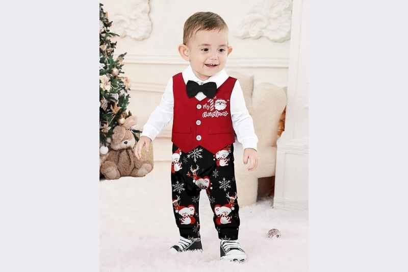 Baby boy standing while wearing the AGAPENG My First Christmas Gentleman Romper with bow tie and vest, surrounded by Christmas decorations, glowing holiday lights, and festive background décor; formal newborn and infant baby boy Christmas outfit for photoshoot, 0–3 months to 1-year holiday pictures, and elegant Christmas portrait styling.