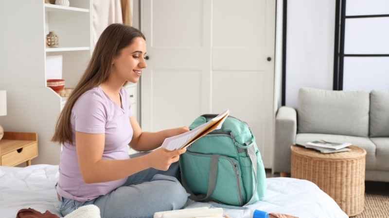 Cesarean Hospital Bag Checklist: pregnant woman in bed with a hospital bag and essential items, including a notebook for last-minute must-haves.