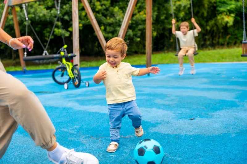 Toddler kicking a colorful ball outdoors, practicing coordination, balance, and gross motor skills through fun toddler outdoor activities.