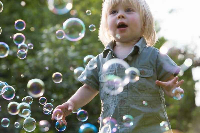 Toddler running and chasing bubbles outside, enjoying playful and fun toddler outdoor activities while developing coordination and gross motor skills.