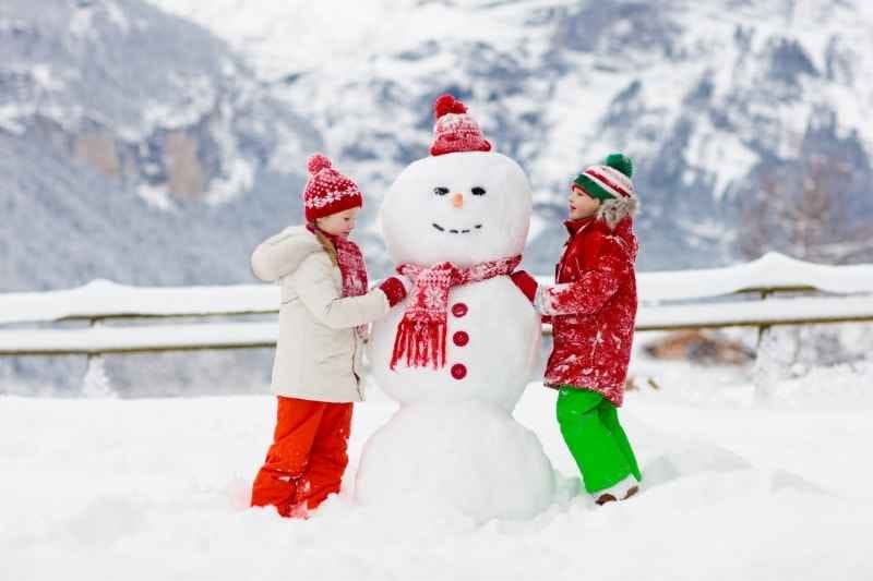 Two toddler rolling snowballs to build a snowman, having fun in the snow while exploring outdoor winter play.
