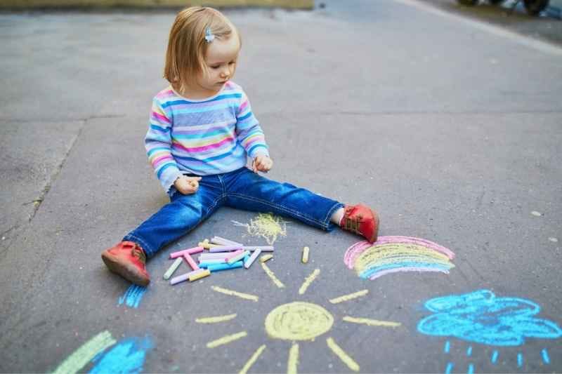 Toddler drawing with colorful chalk outdoors, exploring creativity and fine motor skills through fun toddler outdoor activities.