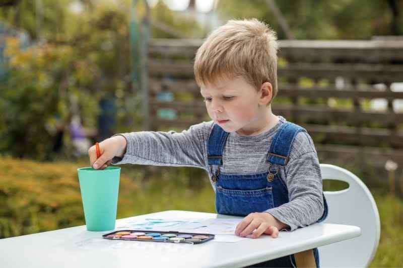 A toddler using colorful ice cubes to paint on the snow, exploring colors and textures outdoors.
