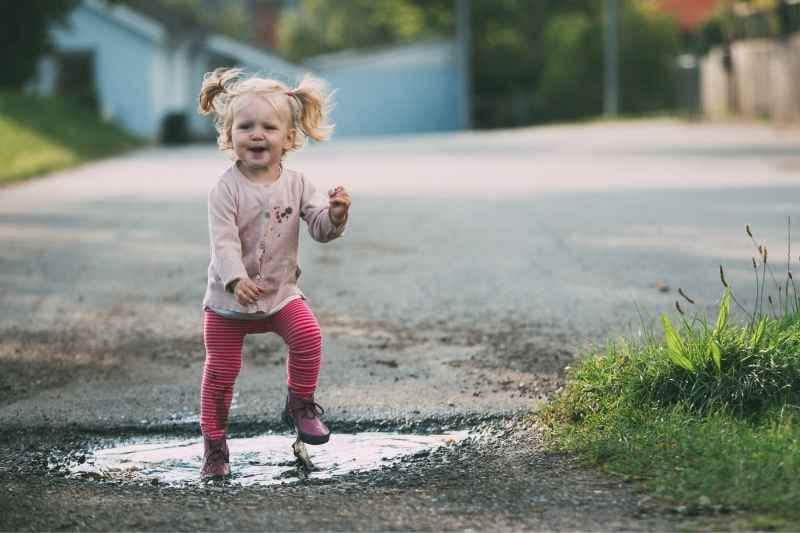 A toddler in bright rain boots joyfully splashing in a puddle on a rainy day.
