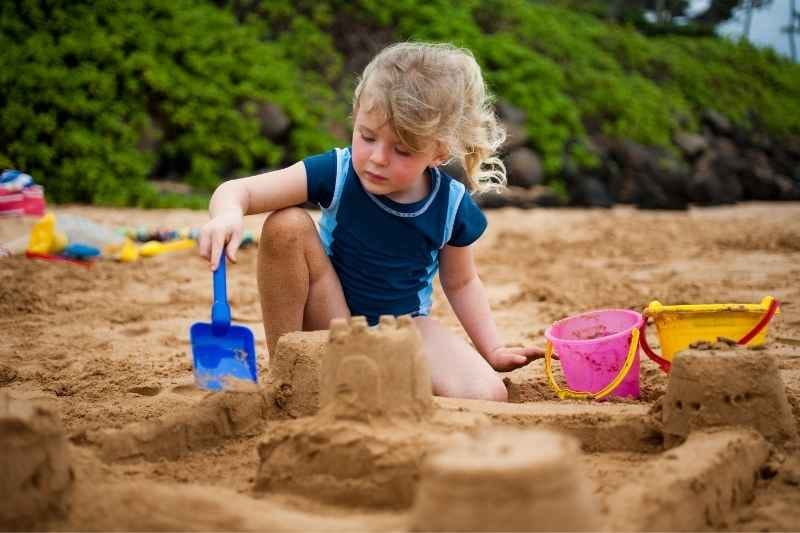 Toddler building a sandcastle outdoors with hands and small tools, enjoying playful and creative toddler outdoor activities.