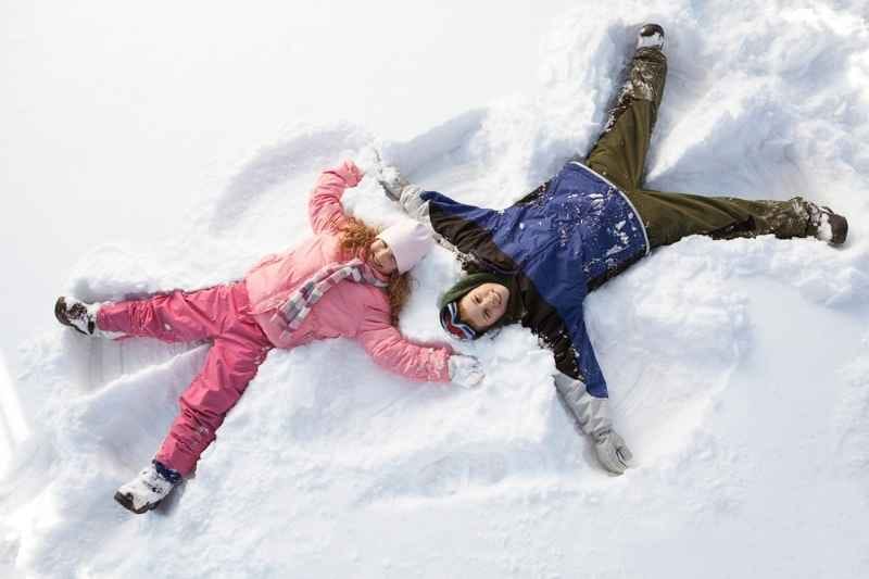 Toddlers lying in the snow, moving arms and legs to create a snow angel.