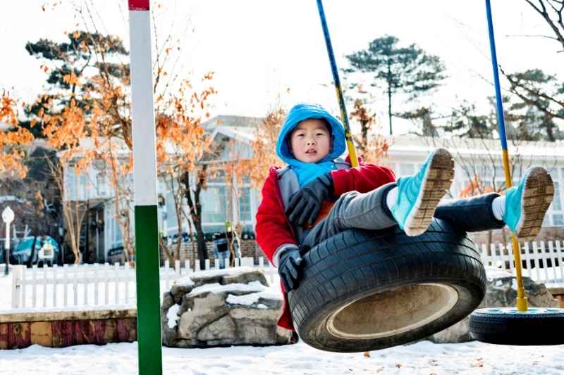 A toddler enjoying a gentle swing on a tire swing in a snowy backyard, smiling and holding on tightly.